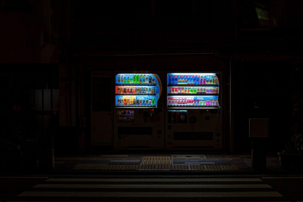 Brightly lit vending machines on a dark street at night, highlighting urban convenience.